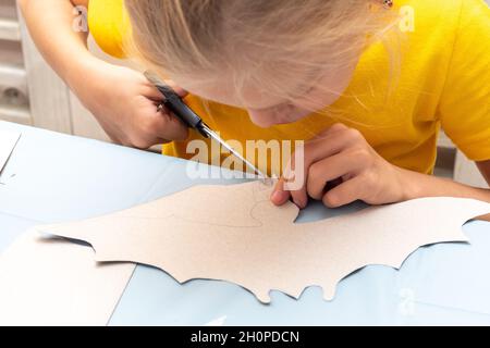 Una ragazza taglia una decorazione di Halloween a casa da carta nera. Fai da te artigianato decorazioni per la casa. Il bambino fa i mestieri di carta, origami Foto Stock