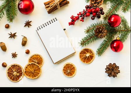 Layout del notebook per registrare il testo. Vista dall'alto del layout piatto di fette di arancio, noci, palline e rami di abete rosso e bacche Foto Stock