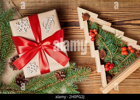 Composizione natalizia di scatola regalo e albero di natale in legno con rami di abete e bacche di rowan all'interno su sfondo di legno Foto Stock