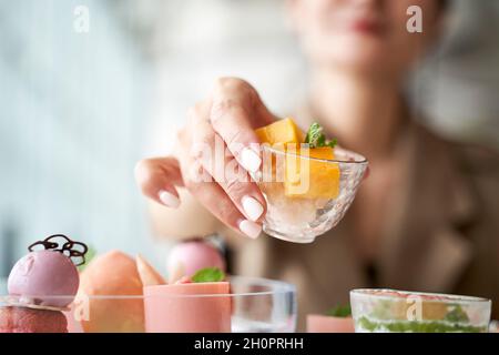 primo piano di mani di una donna asiatica che raccoglie un dessert dal tavolo da pranzo al ristorante Foto Stock