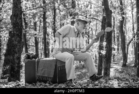 Avere piacere di leggere di più. Pensionato persona leggere libro in autunno natura. Il vecchio uomo leggeva seduta sulla valigia retrò. Letteratura e biblioteca. Conoscenza e. Foto Stock