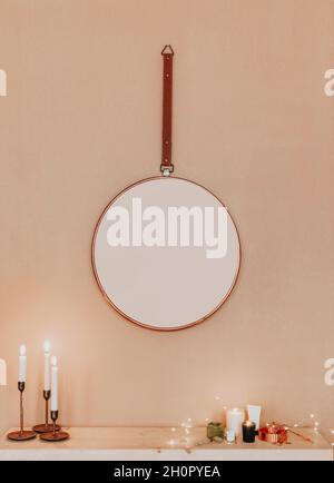 Design minimalista interno di appartamento con specchio rotondo appeso su parete beige, toeletta con candele a legna di vario stile, cosmetici e des Foto Stock