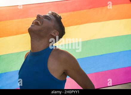 Giovane uomo transgender con trucco sorridente con bandiera arcobaleno lgbt sullo sfondo Foto Stock