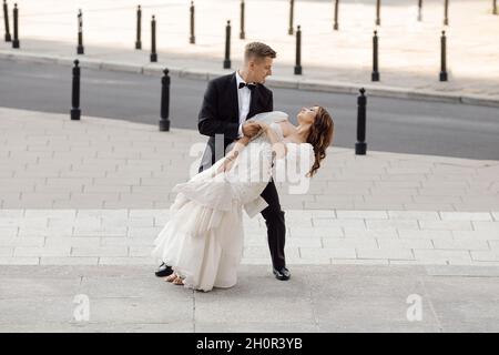 Giovane coppia sposa e sposo, uomo e donna in abito da sposa, ballando in città. Concetto di matrimonio. Momenti felici, a tutta lunghezza Foto Stock