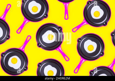 Motivi creativi con uova fritte su padelle rosa su sfondo giallo. Vista dall'alto. Modello creativo in stile minimal. Disposizione piatta. Banner. Foto Stock