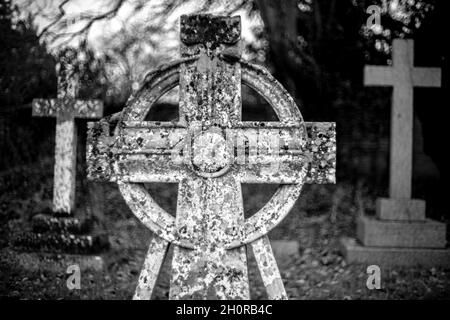 Foto in scala di grigi di una vecchia croce in un cimitero a Cotswolds, Inghilterra Foto Stock