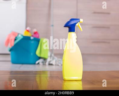Spruzzare una bottiglia di prodotto detergente sul pavimento della cucina con il secchio e l'attrezzatura di pulizia davanti agli armadi sullo sfondo Foto Stock
