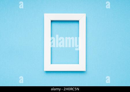 Cornice fotografica bianca in legno su superficie blu, composizione minima, cornice fotografica verticale, spazio per il testo, vista dall'alto Foto Stock