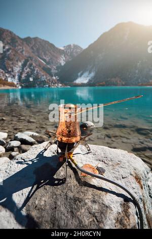 Rame Cezve con caffè su una stufa a gas in autunno lago campeggio in montagna. Preparazione del caffè all'aperto Foto Stock