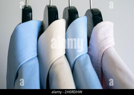 Primo piano di appendiabiti con magliette da lavoro. Fila di camicie colorate su un rack. Appendiabiti in tessuto con camicia uomo casual. Foto Stock