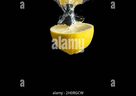 Limone giallo fresco in acqua spruzzata isolato su fondo nero. Concetto di cibo minimo. Foto Stock