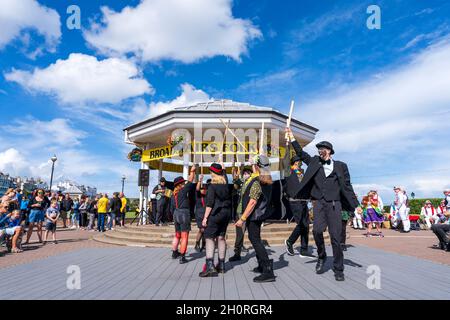 Scopa mattoni e Bowlers Manic Morris uomini ballare di fronte al Bandstand sul lungomare durante l'annuale Broadstairs Folk Week festival. Foto Stock