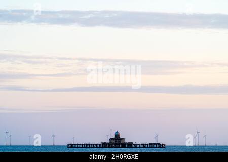 Telefoto delle rovine del molo testa a Herne Bay sulla costa del Kent. Turbine eoliche sullo sfondo, cielo all'alba in color pastello malva e giallo pallido. Foto Stock