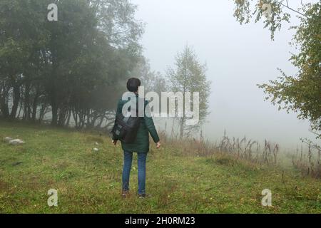 Donna con uno zaino guarda la fitta nebbia in montagna Foto Stock