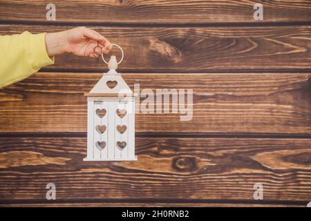 mano di una donna irriconoscibile tiene lanterna di legno con i cuori su uno sfondo di legno. concetto di decorazione da materiali naturali. Giocattoli ecologici per bambini Foto Stock