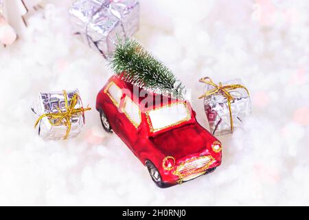 Piccola auto giocattolo rosso retrò con abete verde sulla parte superiore e si presenta su bianco fondo neve artificiale. Festa di Natale e Capodanno Foto Stock