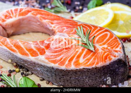 Salmoni rossi crudi fette di pesce con spezie, rosmarino e limone in cucina su sfondo chiaro. Foto Stock