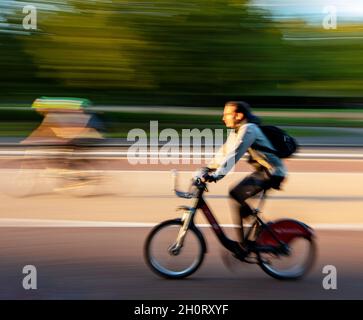 Ciclista su South Carriage Drive, Hyde Park, Londra; movimento veloce che produce immagini sfocate Foto Stock