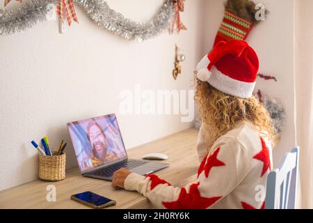 Una donna a casa seduta sul desktop utilizzare il laptop per videochiamare marito via per celebrare insieme natale - persone moderne lontano amano lo stile di vita Foto Stock
