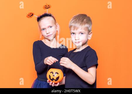 Halloween bambini. Il trucco o il piacere dei bambini è una tradizione di Halloween. Ragazzo e ragazza che tengono un cestino a forma di zucca arancione con dolcetti nelle mani Foto Stock