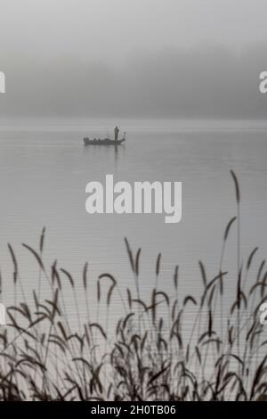 Plainwell, Michigan - Un uomo pesca da una barca sul lago Pine nella nebbia di prima mattina. Foto Stock