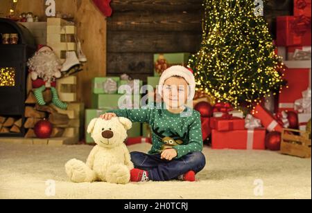 Bambino carino. Piccolo ragazzo giocare vicino albero di natale. Divertimento per bambini a casa. Buon natale a tutti. Natale presente. Vacanze invernali. Il bambino felice festeggia l'anno nuovo Foto Stock