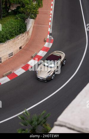 Beige con tetto di borgogna Aston Martin Vanquish Volante supercar guidato su una strada del centro di Monaco, parte del circuito di F1. Foto Stock