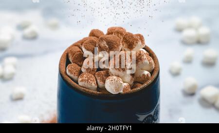 Marshmallow in tazza di caffè con cioccolato in primo piano su sfondo di marmo blu chiaro Foto Stock