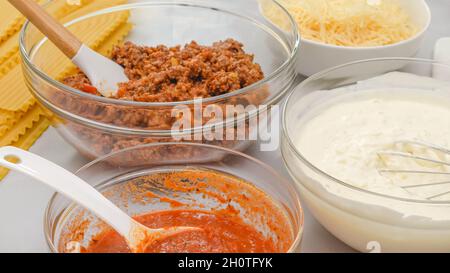 Tagliatelle di lasagna, marinara, manzo macinato, formaggio spalmabile e parmigiano in ciotole. Ingredienti per la ricetta di lasagne di manzo da vicino sul tavolo da cucina. Foto Stock