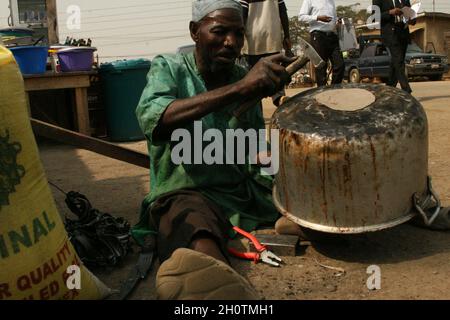 Un artigiano che menda una pentola per strada. Lagos, Nigeria. 8 gennaio 2008. Foto Stock