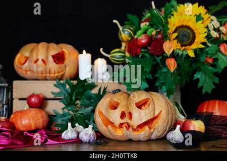 Zucche arancioni con paura jack o'lantern faccia. Autunno Fall concetto: Zucche, candele, girasole, foglie, lanterna e altri attributi al tavolo come sfondo tema Halloween. Foto di alta qualità Foto Stock