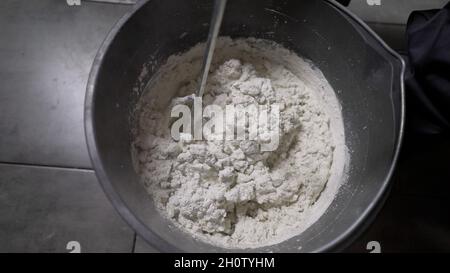 Il mastice di cemento bianco è mescolato in un secchio. Il lavoratore che mescola il gesso in una benna per allineare e stucco pareti dell'appartamento usando un trapano elettrico, Foto Stock