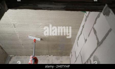 Innesco del soffitto con un rullo. Primer di lavoro con un rullo per verniciatura a soffitto. Primo piano del processo di adescamento del calcestruzzo. Foto Stock