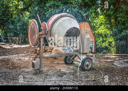 Betoniera, sabbia e ghiaia in un giardino verde Foto Stock