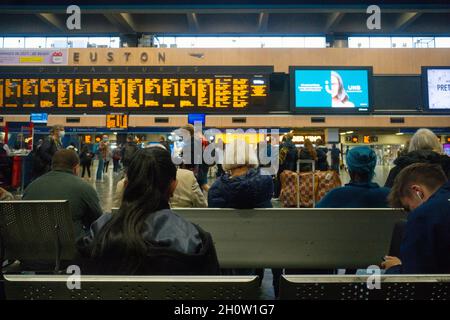 Stazione di Euston in attesa di treni che guardino le partenze durante gli orari più tardi, quindi alcune persone che indossano le coperture facciali Foto Stock