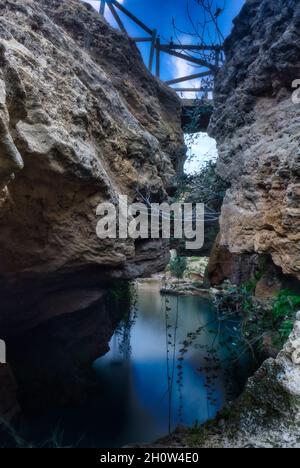 Vista ipnotica di un ponte tra scogliere rocciose su acque lucide sotto un cielo blu nuvoloso Foto Stock