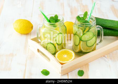 Disintossicare l'acqua con limone e cetriolo tagliati in un vaso su un tavolo di legno. Concetto sano. Foto Stock