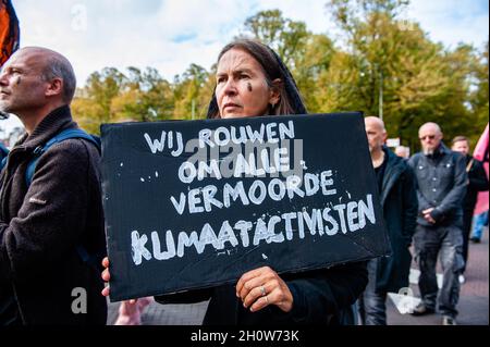 L'Aia, Paesi Bassi. 14 Ott 2021. Una donna ha visto tenere una placard riscaldamento dell'omicidio di attivisti del clima.come parte della nuova campagna di ribellione estinzione Rebellion clima, Centinaia di attivisti del clima hanno camminato in abiti neri intorno al centro dell'Aia come processione funebre per onorare la memoria delle vittime del cambiamento climatico e della crisi ecologica. La processione silenziosa fu fatta guidare dai ribelli neri e passò da diversi uffici politici di partito della città. Credit: SOPA Images Limited/Alamy Live News Foto Stock