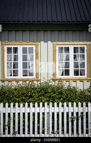 Hafnarfjordur, Islanda - 17 luglio 2021: Primo piano di un cottage islandese tradizionale. Parete bianca, due finestre e una recinzione in legno bianco. Foto Stock