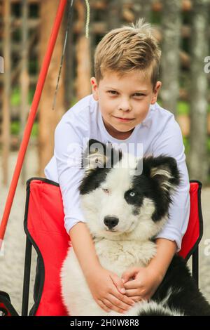 Ragazzo in abiti bianchi abbracciando una soffice razza di cani Husky seduta Foto Stock