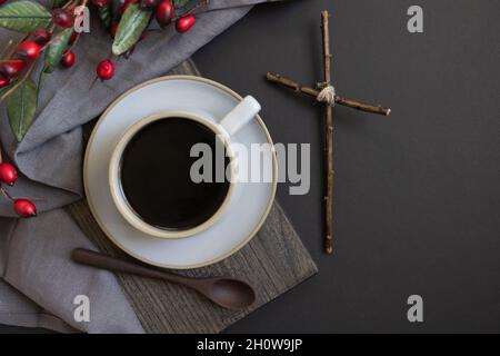 Tazza di caffè e croce di legno con bordo di Natale su sfondo nero con spazio copia Foto Stock