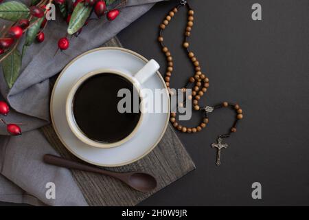 tazza di caffè nero e rosario in legno con bordo rosso di acino su sfondo nero Foto Stock