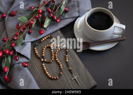 tazza di caffè nero e rosario in legno con bordo rosso di acino su sfondo nero Foto Stock