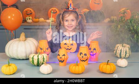 La strega piccola conjura le zucche su Halloween. Fumo colorato sotto la bacchetta magica. Una ragazza piccola felice vestita come una strega gioca la stregoneria di un sorc Foto Stock