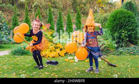 Le streghe piccole imparano a volare i bromoomsticks ad una festa all'aperto di Halloween. I bambini felici in costumi di carnevale con palloncini hanno divertimento e giocare le streghe dentro Foto Stock