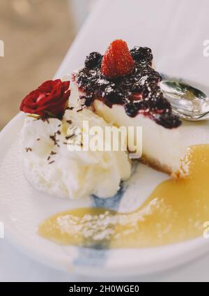 Una porzione di cheesecake con bacche rosse e panna Foto Stock