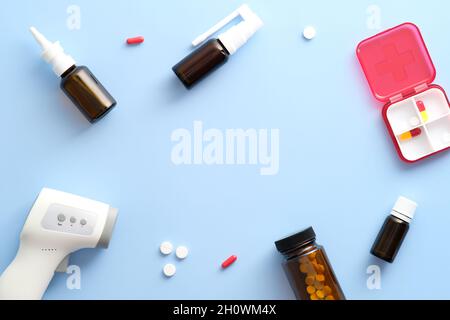 Composizione di posa piatta per uso medico. Cornice in termometro a infrarossi, gocce nasali, spray, pillole su sfondo blu. Covid-19, concep per il trattamento del coronavirus Foto Stock