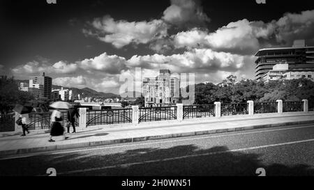 I pedoni attraversano il ponte sul fiume Motoyasu passando per le rovine della cupola della bomba atomica vicino alle bombe atomiche Ground zero a Hiroshima, Giappone. Foto Stock