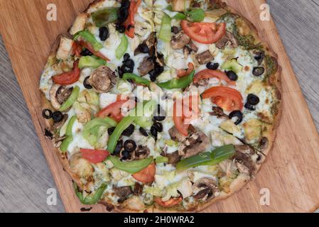 Vista dall'alto della pizza alla crosta di cavolfiore appena sfornata con condimenti di verdure tritati serviti su un piatto di legno. Foto Stock