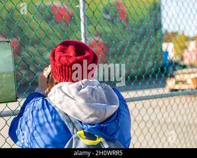 Una donna che guarda attraverso la rete di recinzione del filo. Vista strada, foto di viaggio, sfondo sfocato. Foto Stock